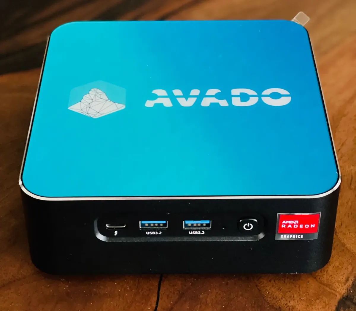 An AVADO box on a wooden desk: a small black computer with a blue lid and the AVADO logo.